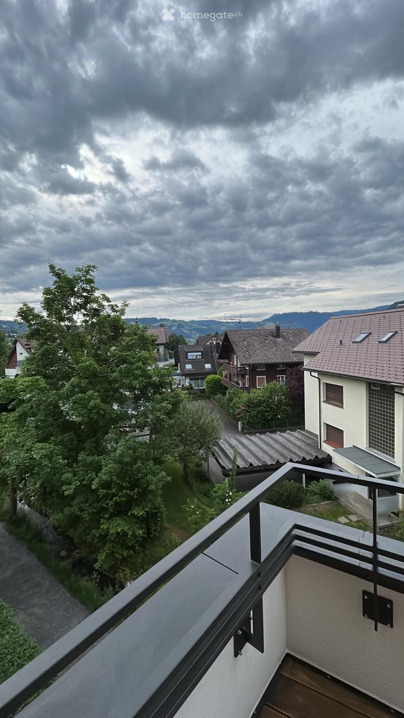 Balcony overlooking a residential area with houses, trees, and a cloudy sky.