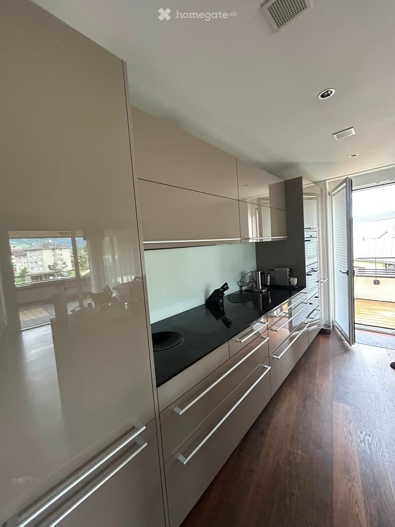Modern kitchen with light-colored cabinets, black countertop, induction cooktop, and small appliances. Open sliding door leads to a balcony.