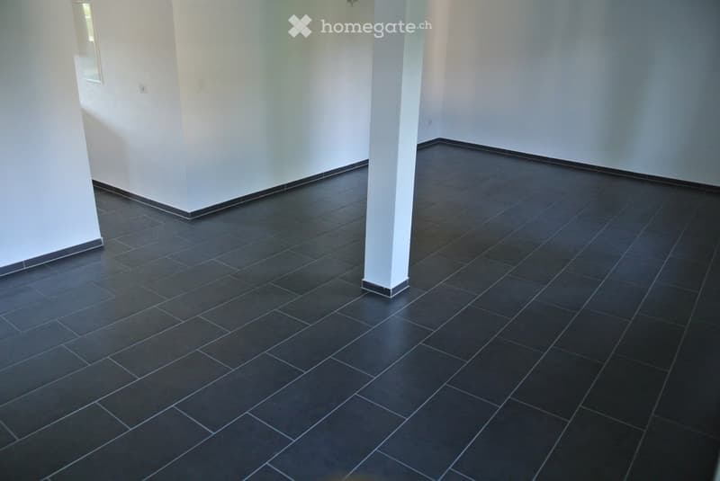 Empty room with dark tiled floor and white walls, featuring a central column and visible electrical outlets.