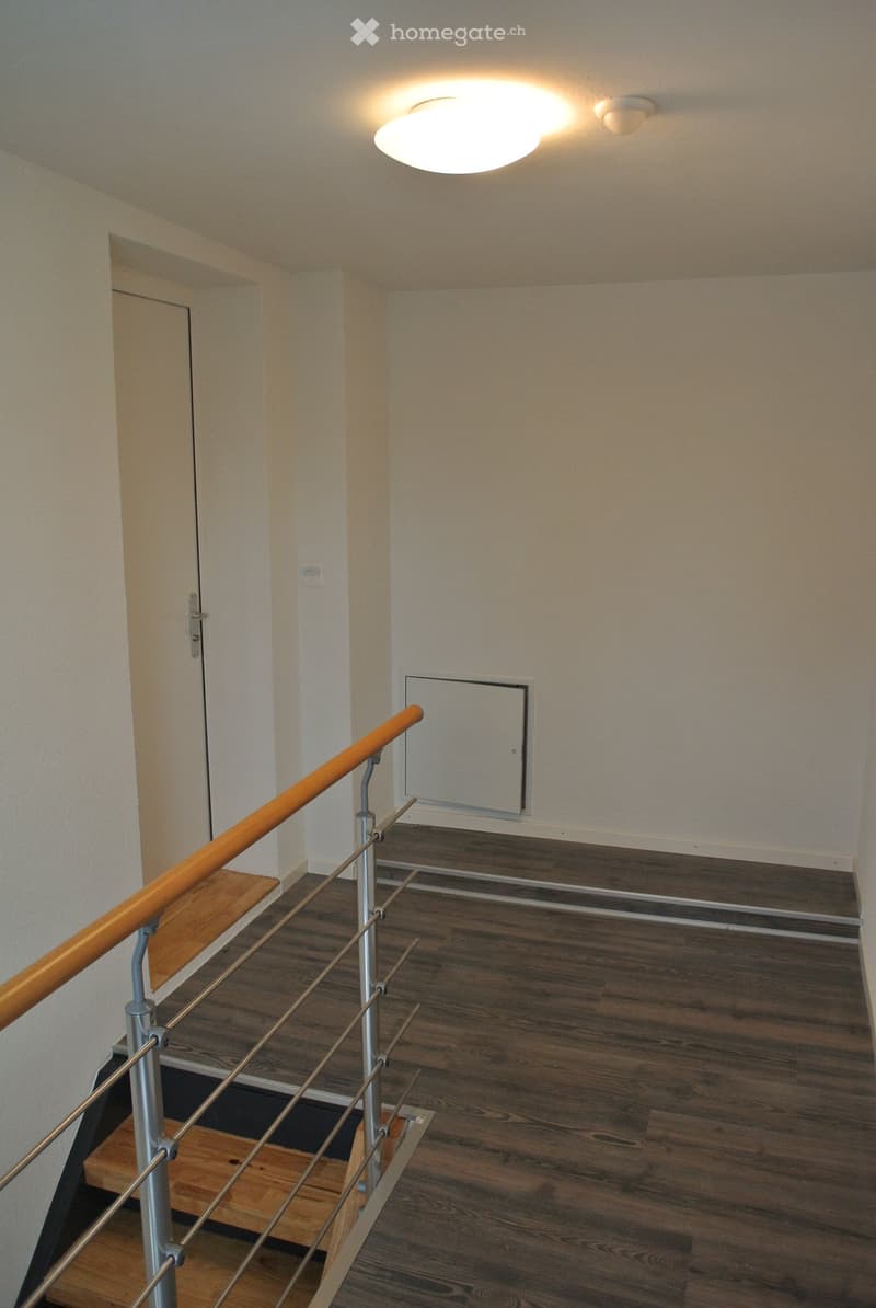 Modern hallway with wooden flooring, a staircase with a wooden handrail and metal balustrade, and a recessed ceiling light.