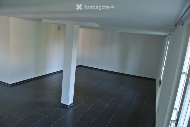 Empty room with white walls, dark tiled floor, and a central column. No furniture or equipment visible.