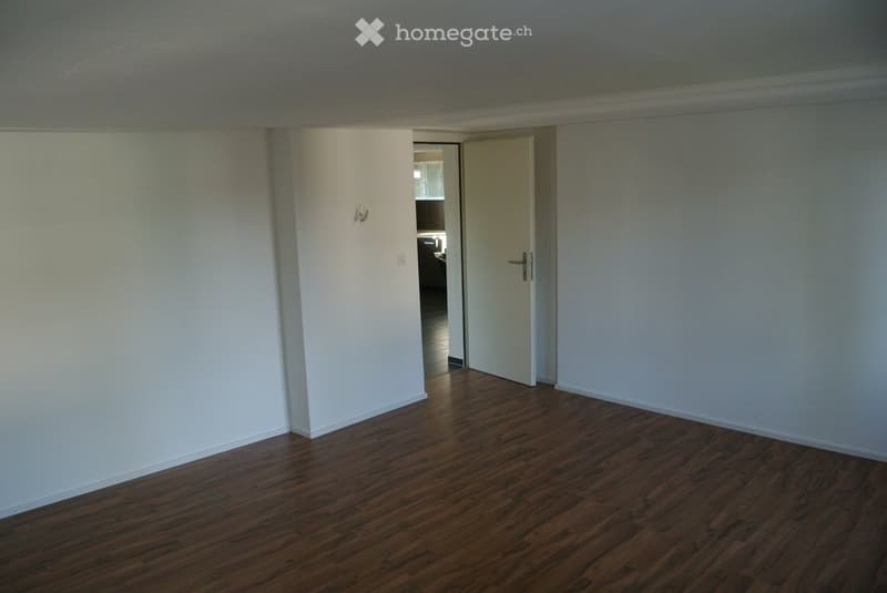 Empty room with wooden flooring and white walls, featuring a partially open door leading to another room.