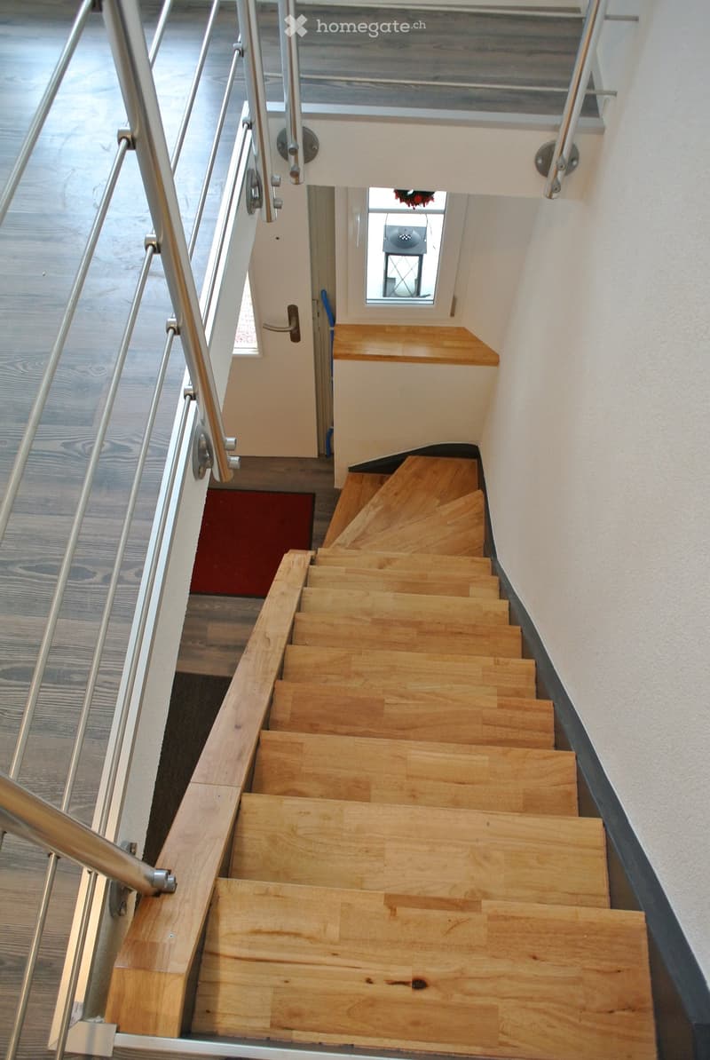 Wooden staircase with metal handrails, leading to a landing area with a small window and a door.