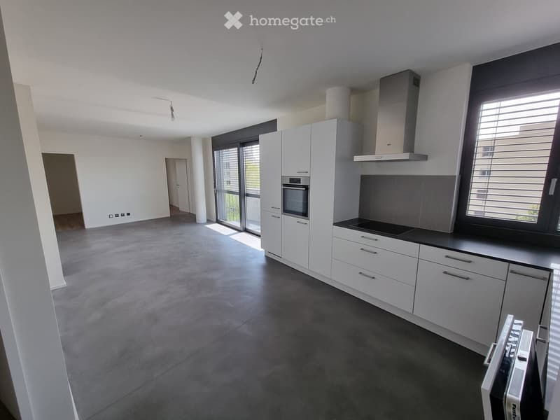 Modern kitchen with white cabinets, stainless steel appliances, and a black countertop. Features a large window and sliding glass door leading to a balcony.