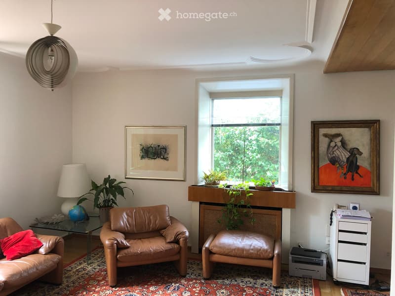 Living room with a leather sofa, armchair, glass coffee table, globe, potted plants, artwork, and a printer on a cabinet.