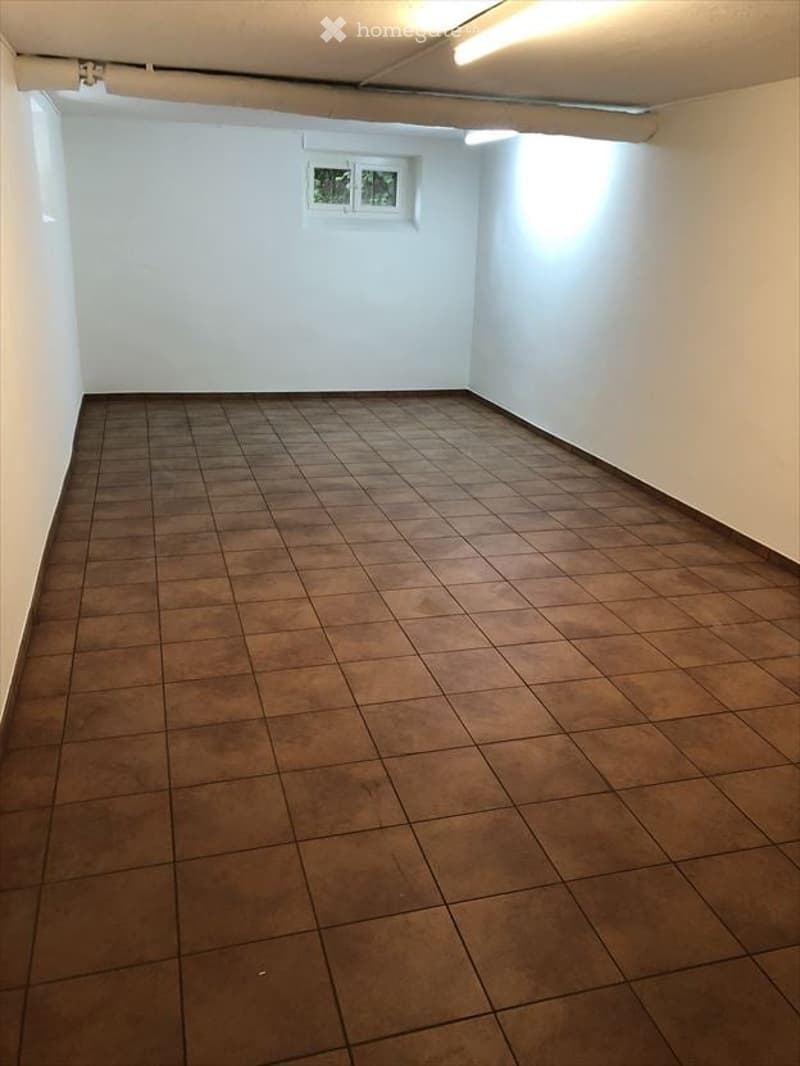Empty room with brown tiled floor and white walls, featuring a small window at the back.