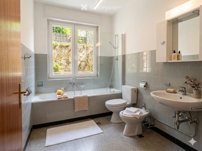 Modern bathroom with a bathtub, toilet, sink, mirror, and shower. Features grey tiles, a window with a view, and decorative towels and a small plant on the sink.
