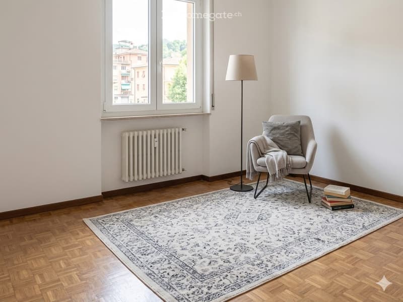 Minimalist living room with a single armchair, floor lamp, and a stack of books on a patterned rug.