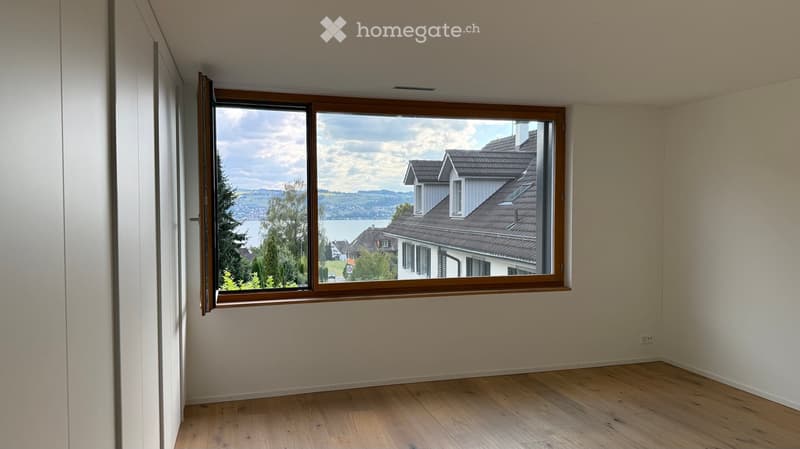 Empty room with wooden flooring, light-colored walls, and a large window offering a scenic view of a house and landscape.