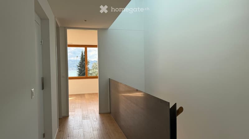 Bright hallway with wooden flooring, white walls, and a large window offering a scenic view of a lake and mountains.