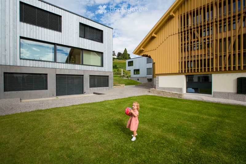 A well-maintained lawn in front of modern residential buildings, with a child playing with a ball.