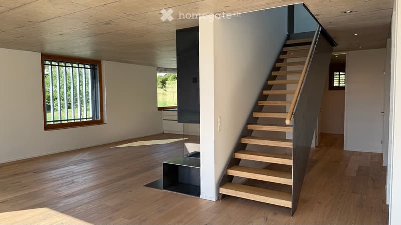 Modern hallway with wooden flooring, a sleek staircase with wooden steps and a metal railing, large windows with wooden frames, and white walls.