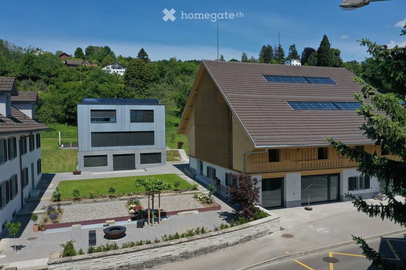 Modern two-story house with a sloped roof, solar panels, and a well-maintained garden area with a fire pit and seating.
