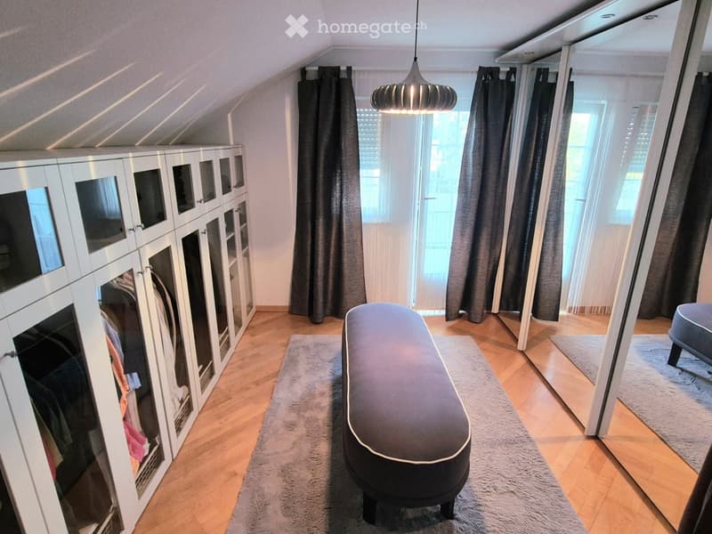 Attic room with wooden flooring, large windows with curtains, built-in wardrobe, bench, and pendant light.