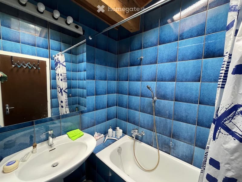 Bathroom with blue tiles, a white sink, a bathtub with a handheld shower, a mirror, and a shower curtain.