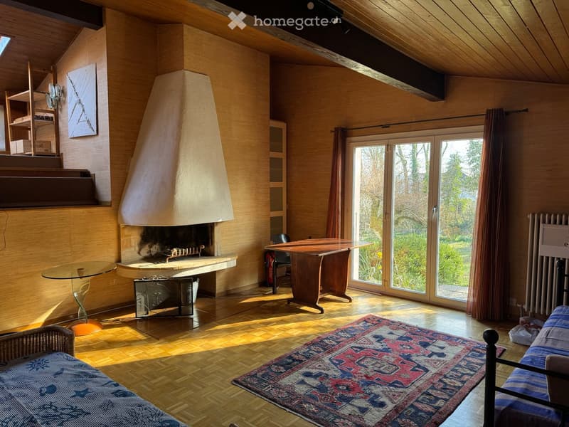 Cozy living room with wooden walls and ceiling, fireplace, large windows, sofa, table, and shelves.
