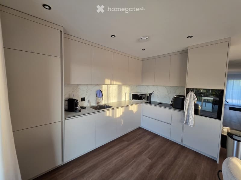 Modern kitchen with white cabinets, wooden flooring, and stainless steel appliances including a sink, microwave, coffee maker, and toaster.