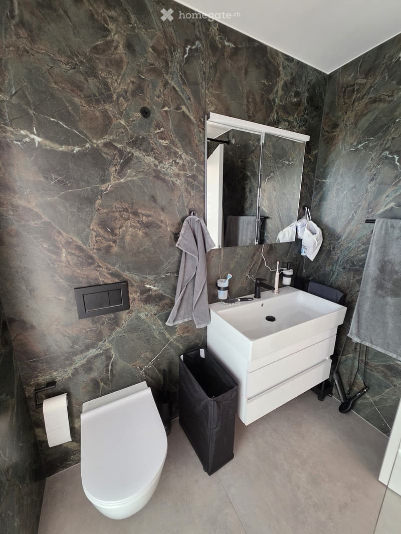 Modern bathroom with marble walls, white sink, toilet, mirror, and towels.