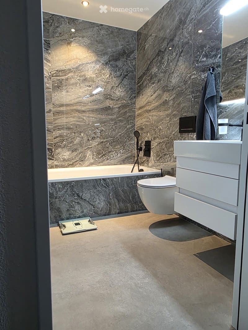 Modern bathroom with marble walls, a bathtub, toilet, sink, and a towel hanging on the wall.