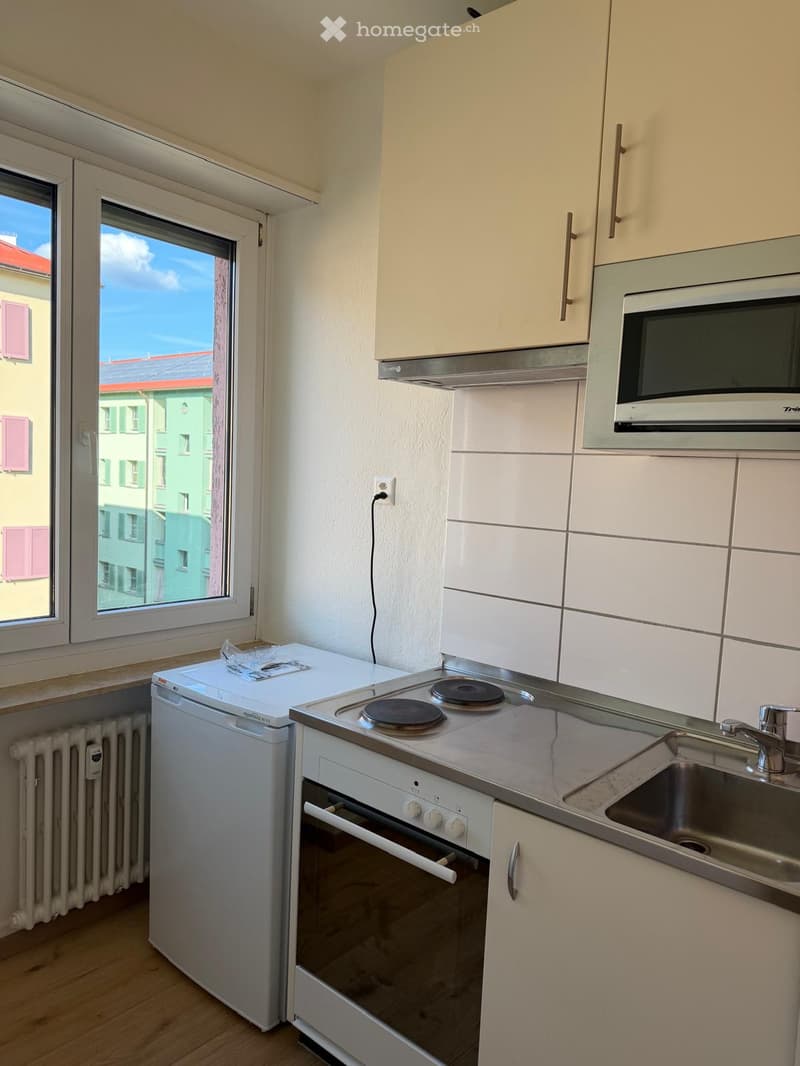 Modern kitchen with white cabinets, stainless steel appliances, and a large window overlooking a cityscape.