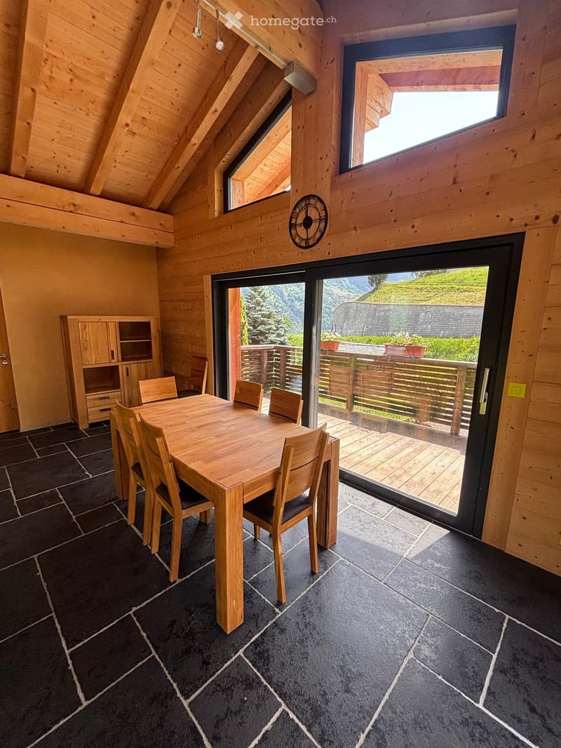Wooden dining area with a table, six chairs, and a cabinet, featuring large windows and a view of the outdoor deck.