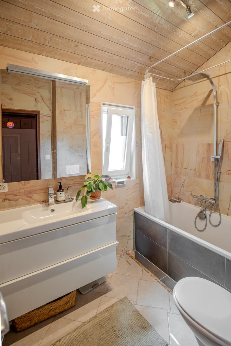 Modern bathroom with wooden walls and ceiling, large sink, bathtub, toilet, and a window letting in natural light.