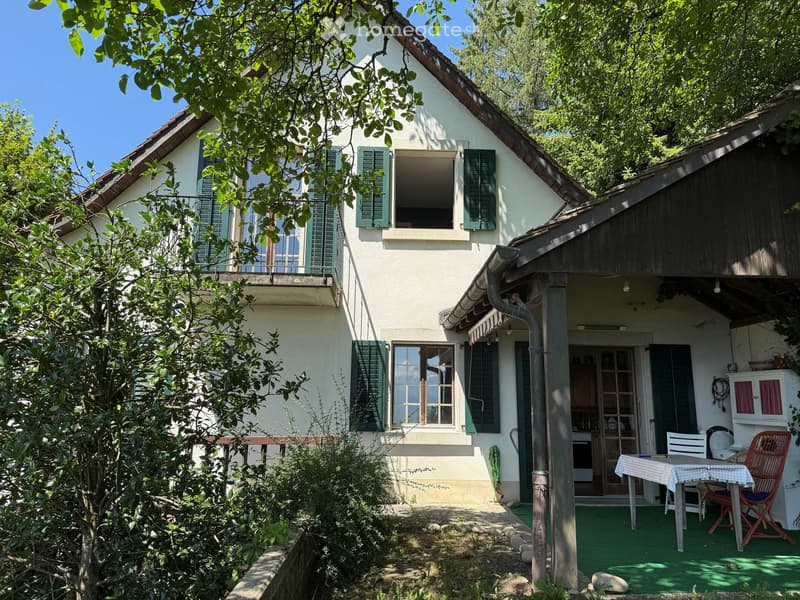 Two-story house with white walls, green shutters, and a covered patio area with outdoor furniture.