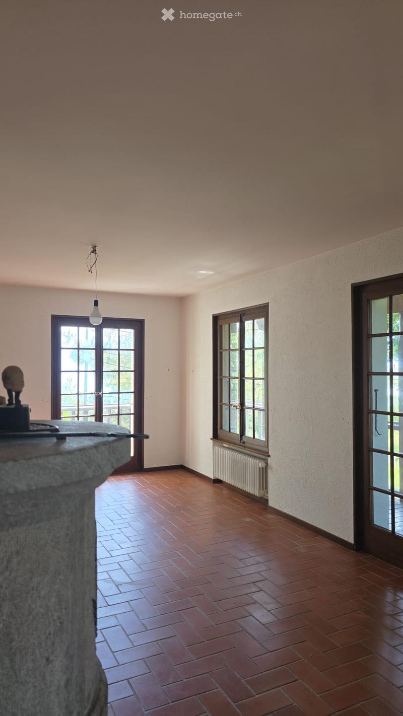 Empty room with wooden tiled floor, large windows, and a radiator. No furniture or equipment present.