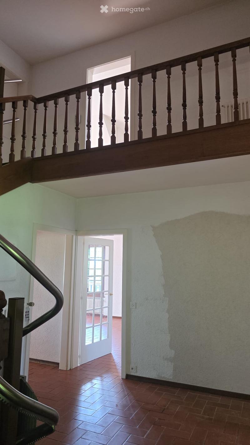 Staircase with wooden railings and a landing leading to an open doorway with glass panels, revealing a tiled floor and part of another room beyond.