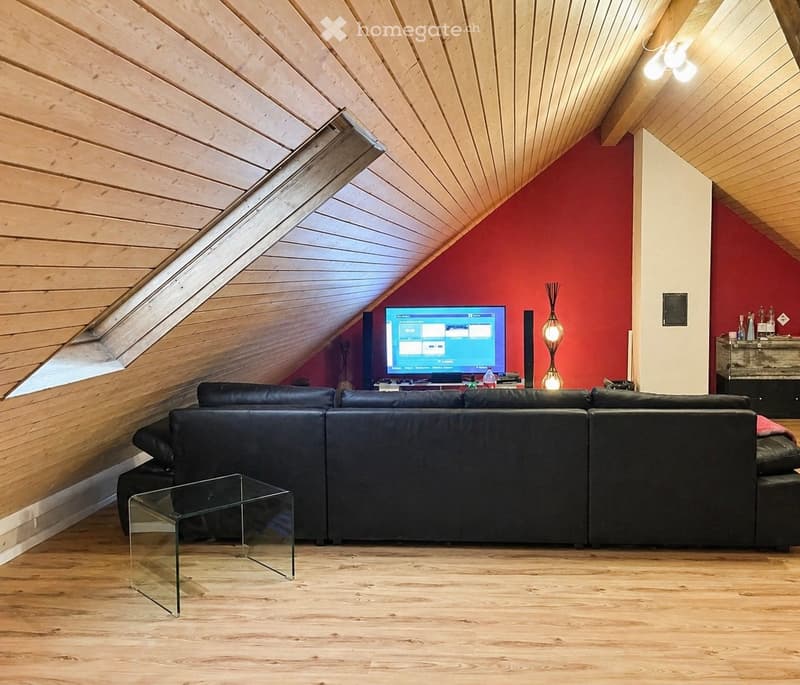 Modern living room with wooden ceiling and floor, red accent wall, black leather sofa, glass coffee table, TV, and floor lamp.