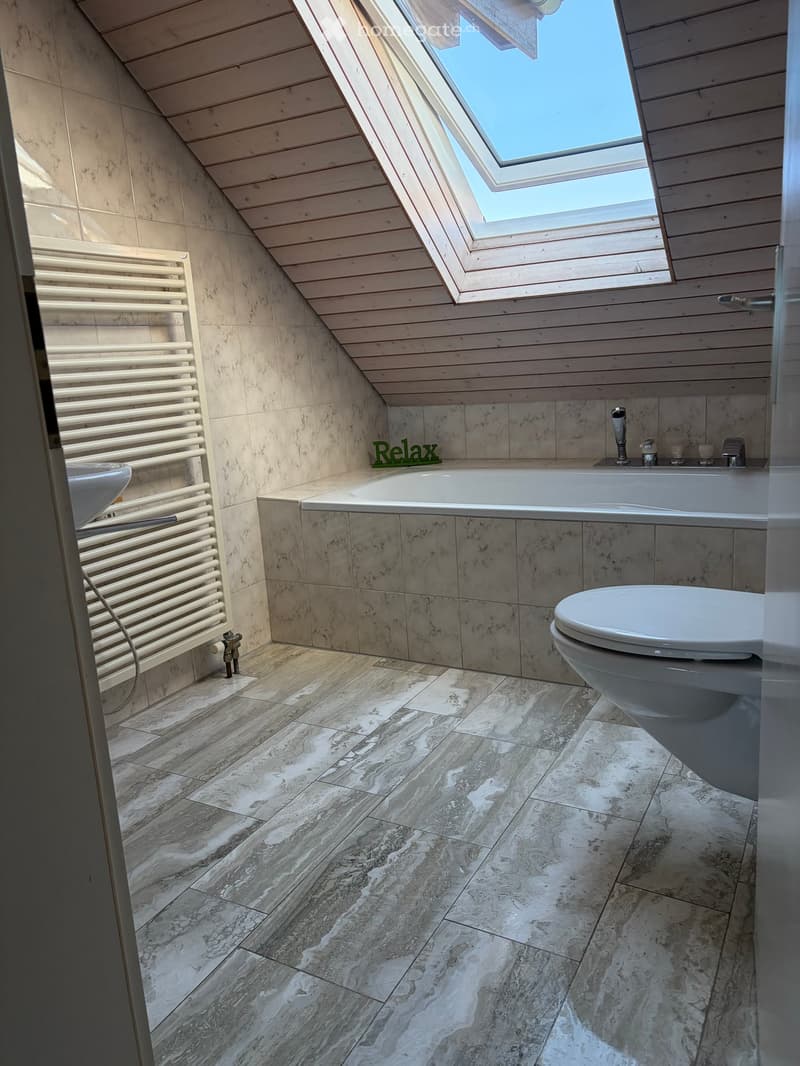 Modern bathroom with marble tiles, a bathtub, toilet, sink, and a radiator. Features a skylight window and a sleek design.