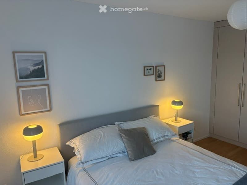 Modern bedroom with a neatly made bed, two nightstands with lamps, and several picture frames on the wall.