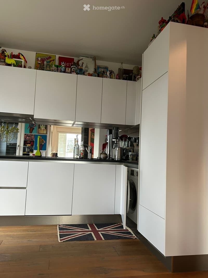 Modern kitchen with white cabinets, stainless steel appliances, and a Union Jack rug on the wooden floor.