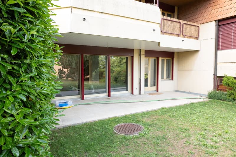 Two-story building with a balcony, large windows, and a small garden area.