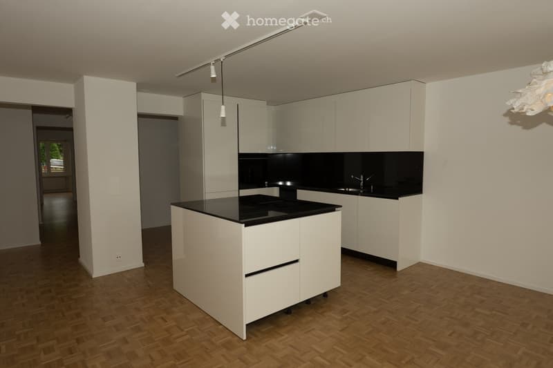 Modern kitchen with white cabinets, black countertops, and a central island. Features include a sink, faucet, and track lighting.