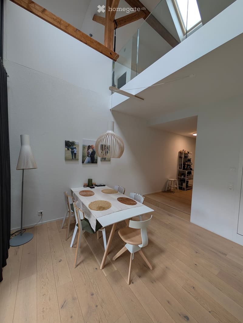 Dining area with a white dining table, six chairs, a floor lamp, and a small cabinet with stools in the background.