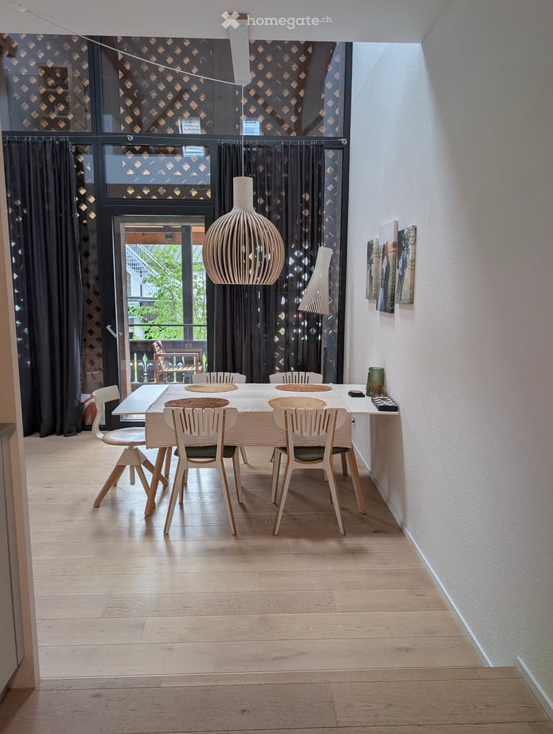 Dining room with a white dining table, six chairs, a large pendant lamp, and a view to a balcony through large windows with dark curtains.