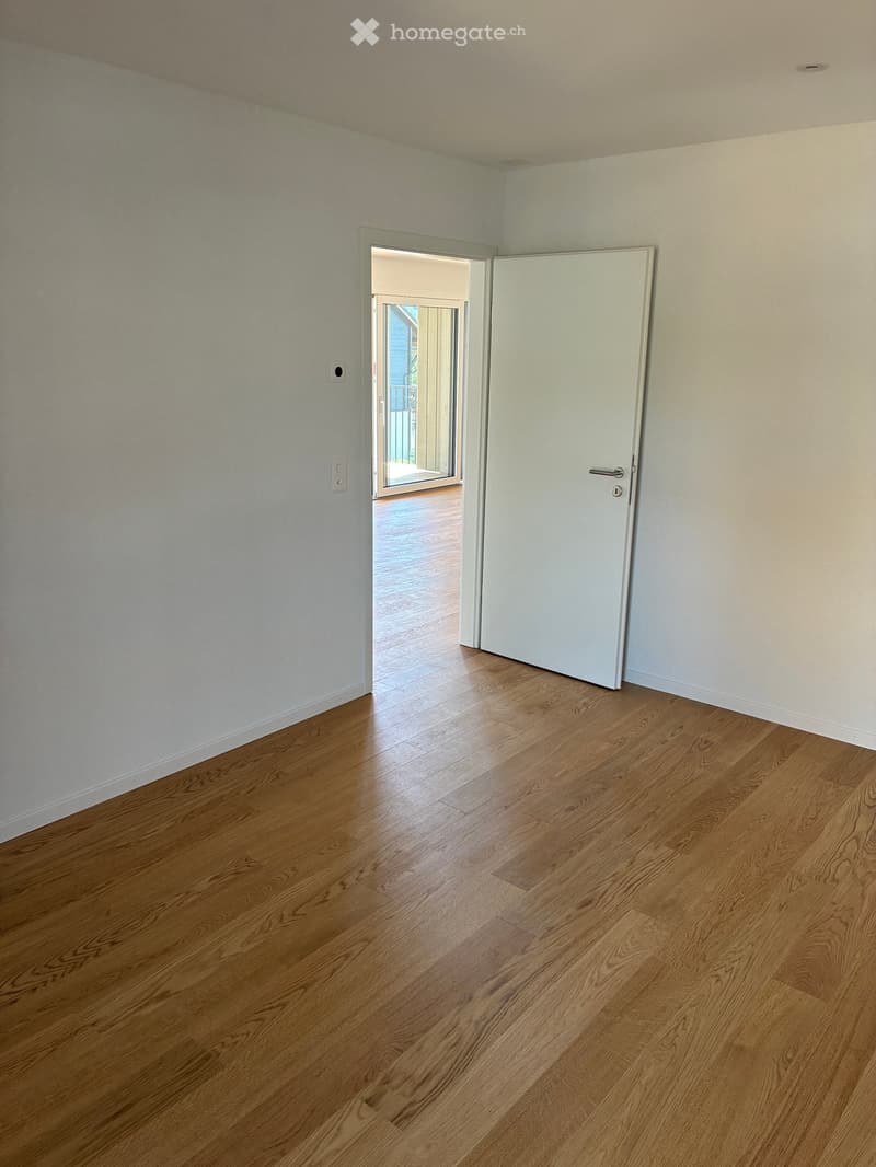 Empty room with light-colored walls and wooden flooring, featuring a white door and an open doorway leading to another space.