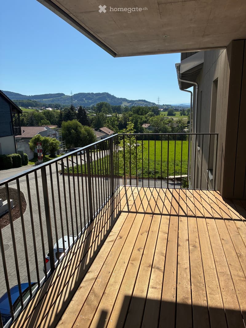 Wooden balcony with metal railing, overlooking a green landscape and distant hills.