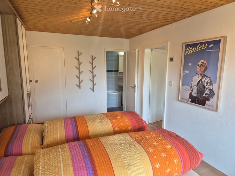 Bright bedroom with a double bed, colorful striped bedspread, a large poster on the wall, and a small bathroom visible through an open door.