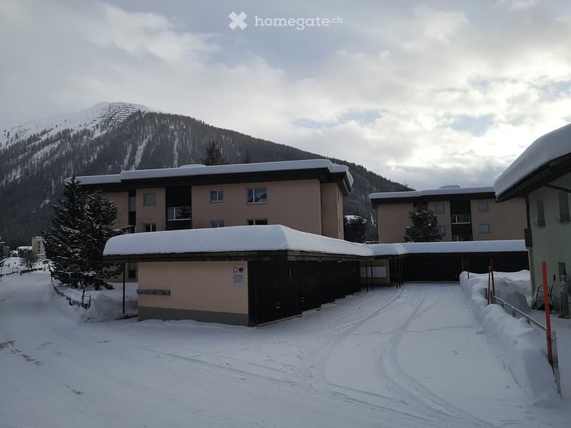 A snow-covered building complex with multiple structures, surrounded by snow-covered trees and mountains.