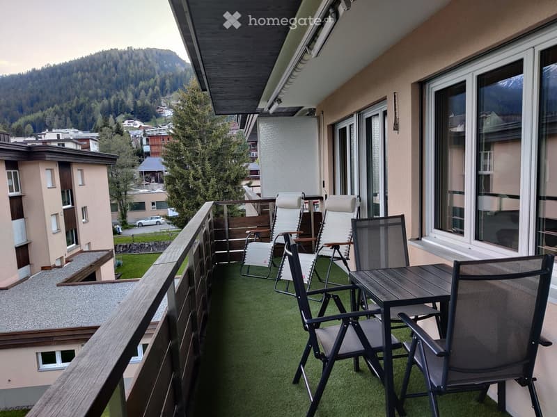 Balcony with artificial grass, wooden railing, and outdoor furniture including a table and chairs.