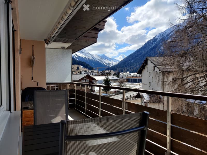 Balcony with wooden railing, metal chair, and scenic mountain view.