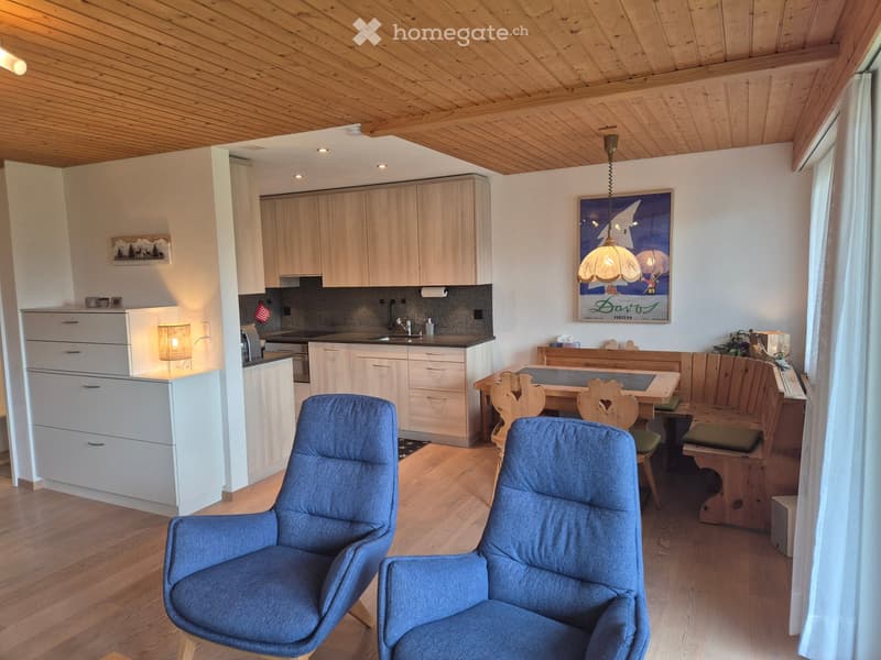 A cozy, well-furnished room with wooden floors, a kitchen area, and a living area. Features include a sofa, chairs, a dining table, cabinets, and a sink.