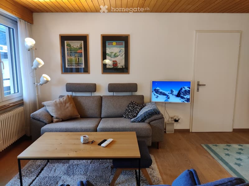 Modern living room with a grey sectional sofa, wooden coffee table, flat-screen TV, floor lamp, and two picture frames on the wall.
