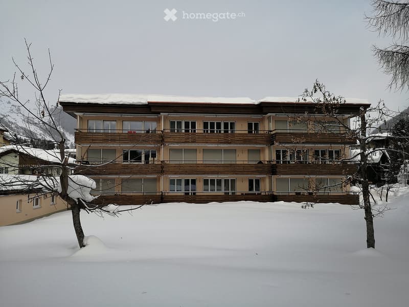 A multi-story building with balconies and snow-covered surroundings, likely a hotel or apartment complex.