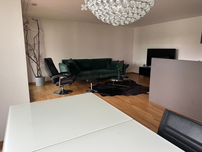 Modern living room with a green sofa, black leather chair, coffee table, and a large white table in the foreground.