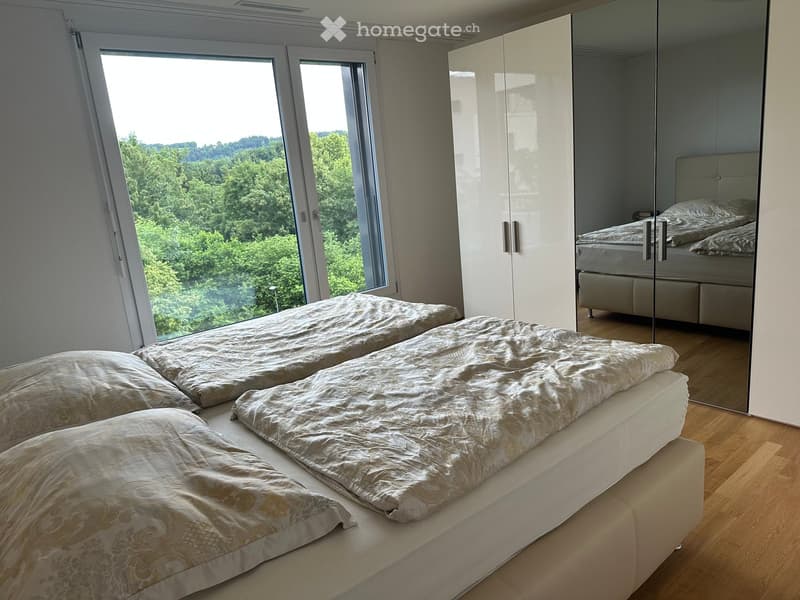 Modern bedroom with large windows offering a scenic view, featuring a neatly made bed and a white wardrobe.