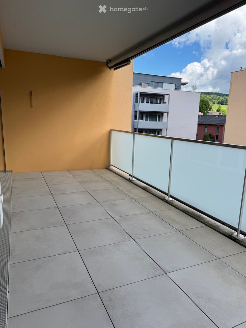Balcony with tiled floor, glass railing, and view of surrounding buildings and landscape.