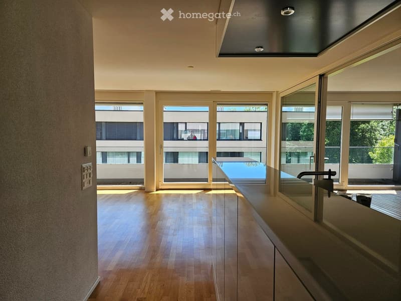 Empty room with wooden flooring, large windows, and a view of a swimming pool and greenery outside.